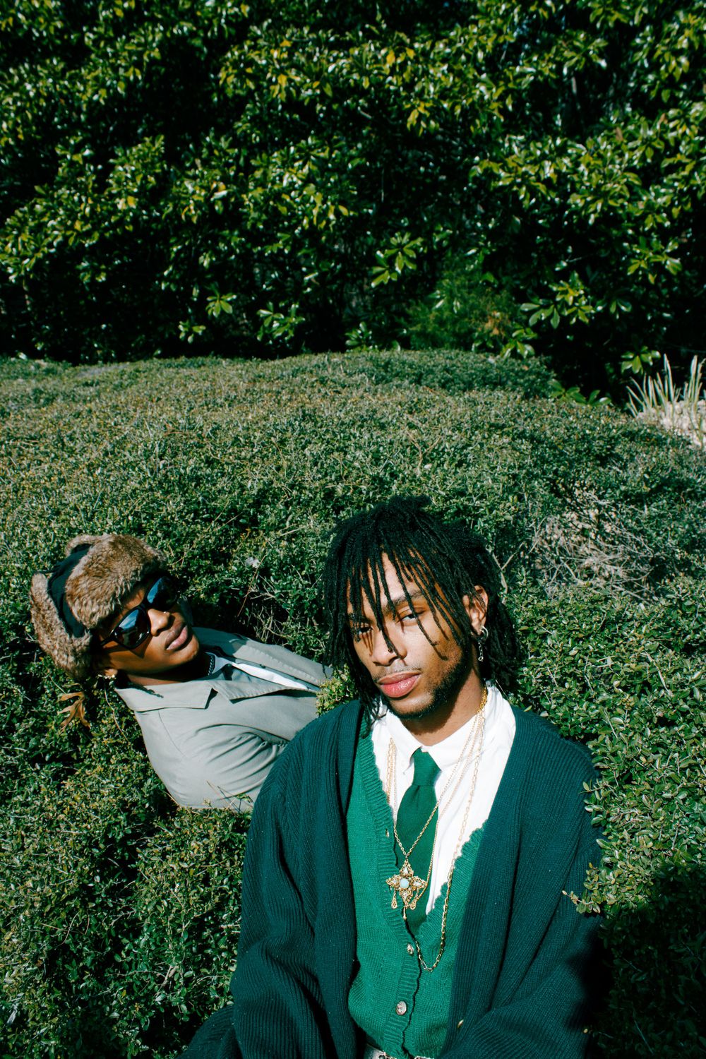 Stylish outdoor fashion shoot in preppy attire against greenery.