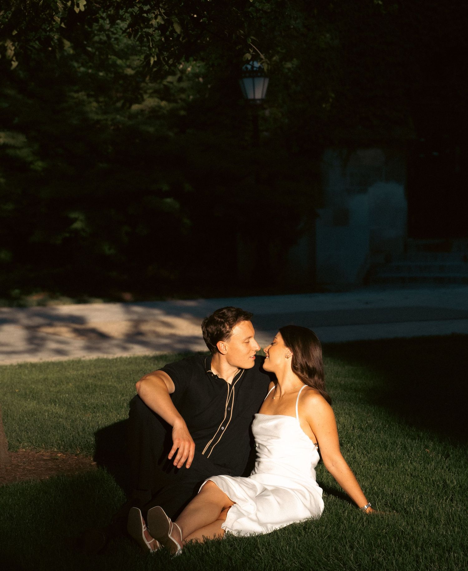 A couple lounges on grass in dappled sunlight during a summer afternoon.
