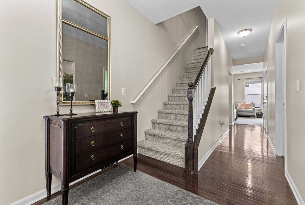 Elegant entryway with dark wood dresser, decorative mirror, staircase, and hardwood floors.