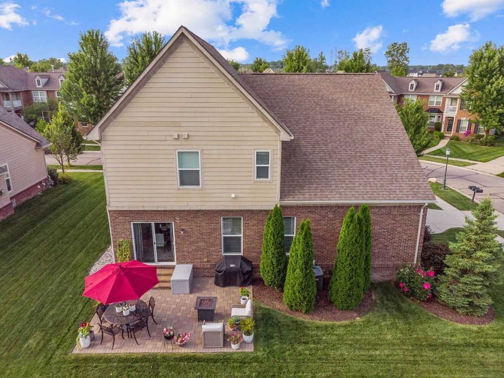 Bird's eye view of two-story brick home featuring patio seating and well-maintained yard.