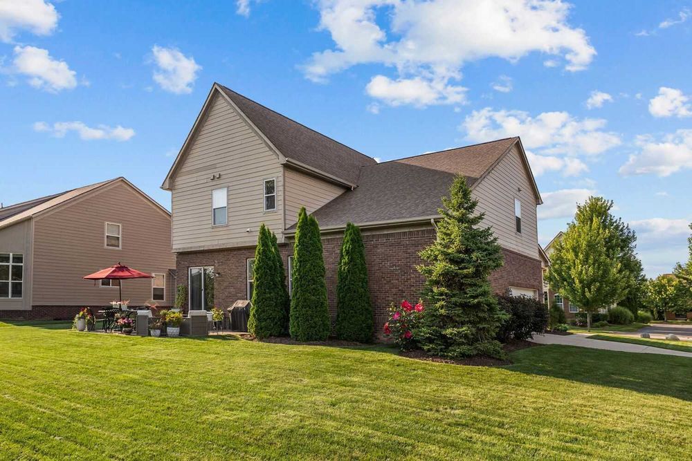 Two-story brick and siding home with lush green lawn and mature landscaping.
