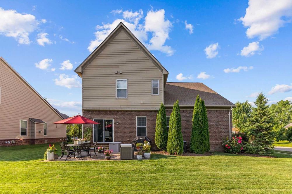 Rear view of two-story brick home with patio, red umbrella, and manicured lawn.