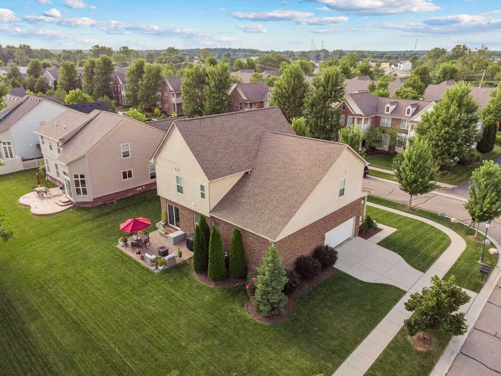 Aerial view of two-story brick home with patio, green lawn, and suburban neighborhood.