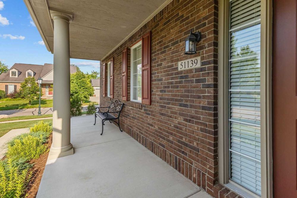 Covered front porch with brick exterior, bench seating, and address number 51139 beside white entry door.