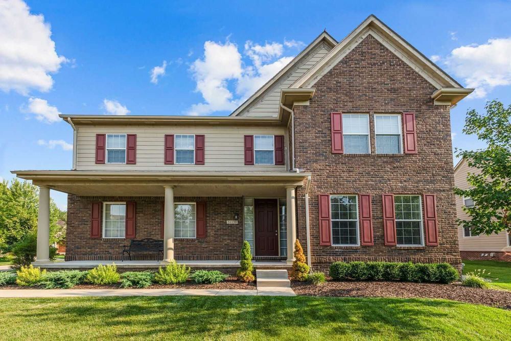 Two-story brick and siding home with covered porch, red shutters, and green lawn.