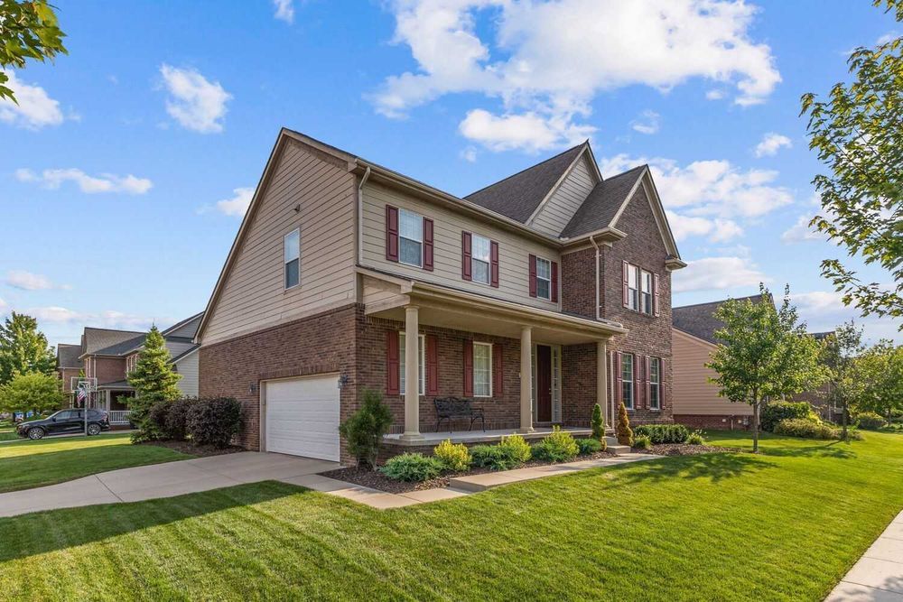Two-story brick and siding home with covered porch, attached garage, and lush green lawn under blue sky.