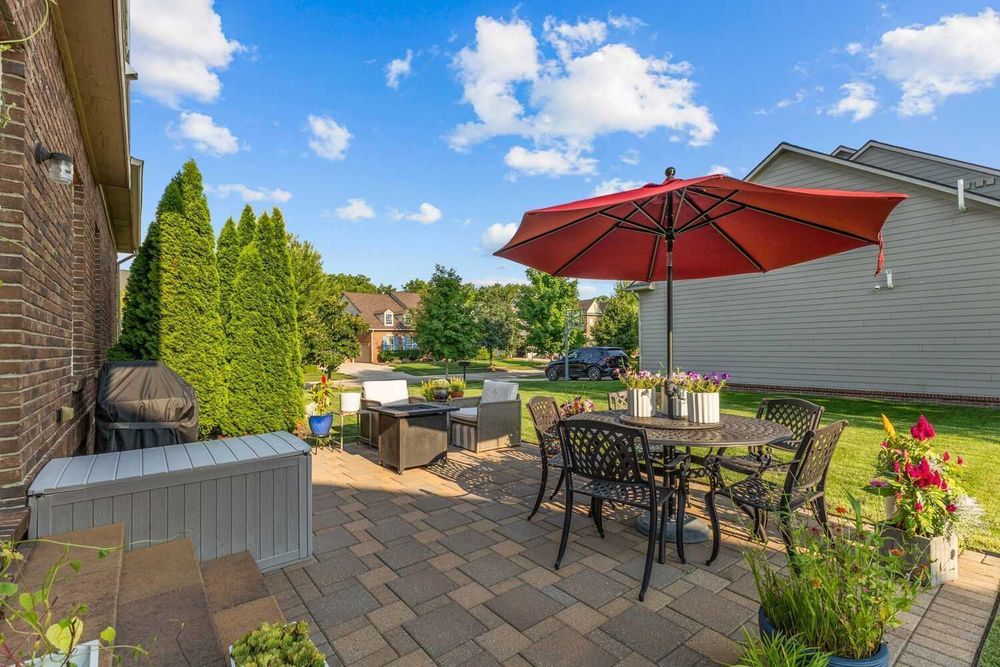 Brick paver patio with outdoor dining set, red umbrella, and lush garden landscaping.
