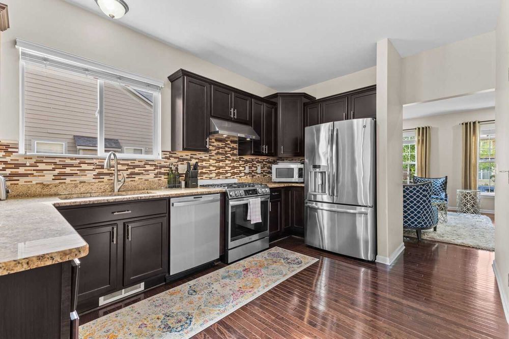 Updated kitchen featuring dark cabinetry, stainless appliances, granite counters, and tile backsplash.