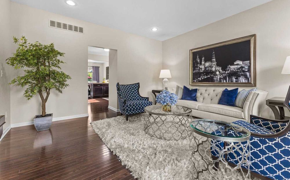 Bright living room with tufted sofa, blue patterned chairs, shag rug, and hardwood floors.