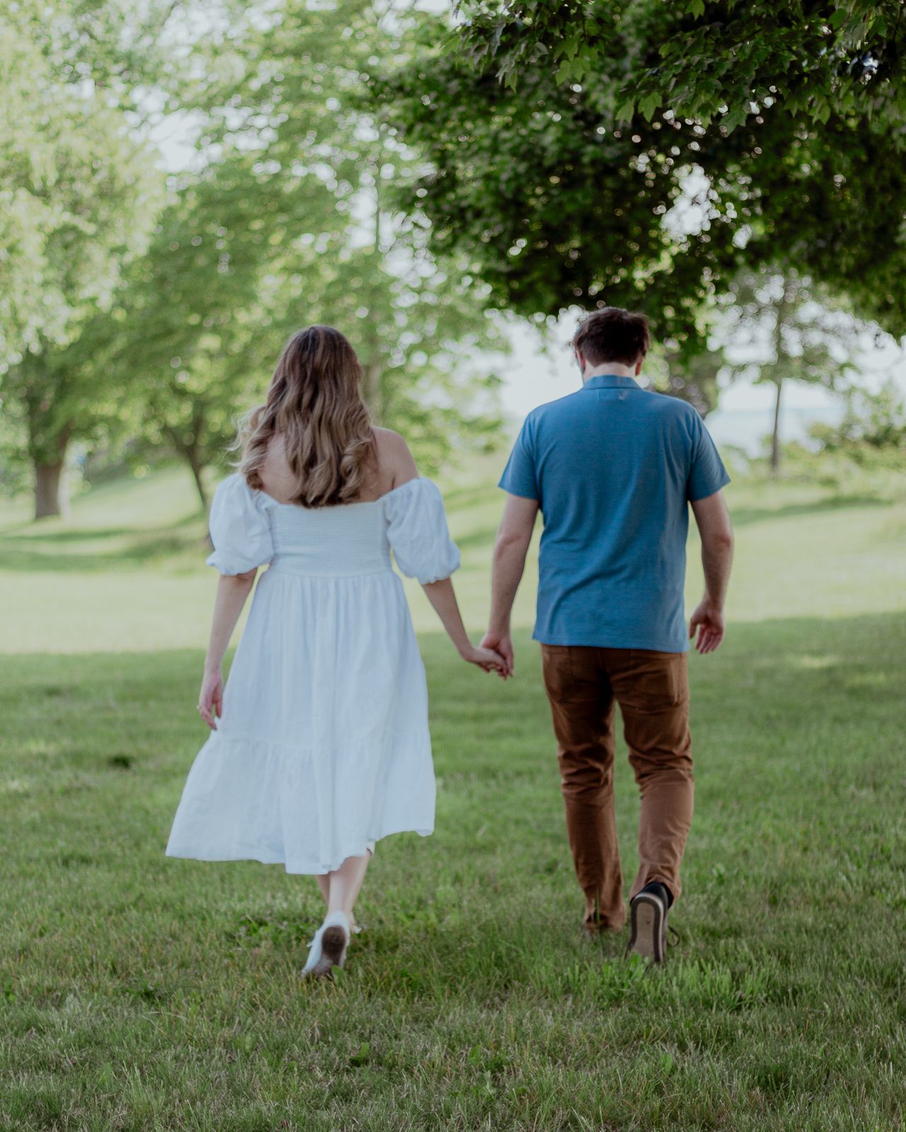 Engagement photography: a couple holding hands and walking away from the camera towards some trees
