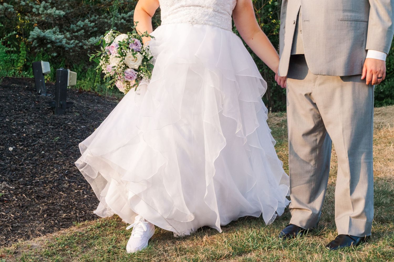 A close-up view of a wedding dress and gray suit during an outdoor ceremony.