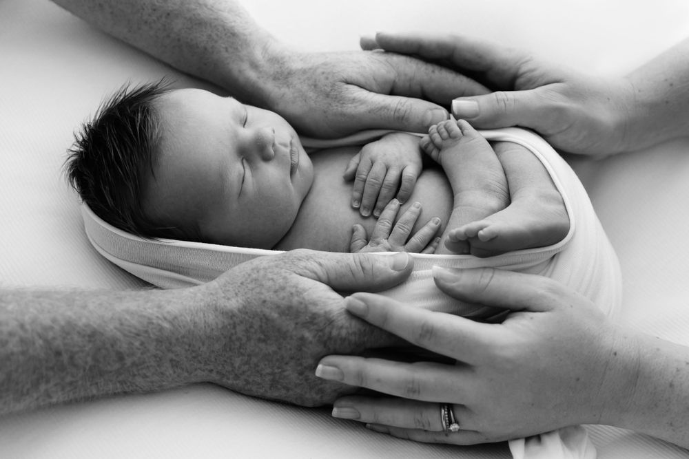 Black and white portrait of sleeping newborn cradled in caring hands.