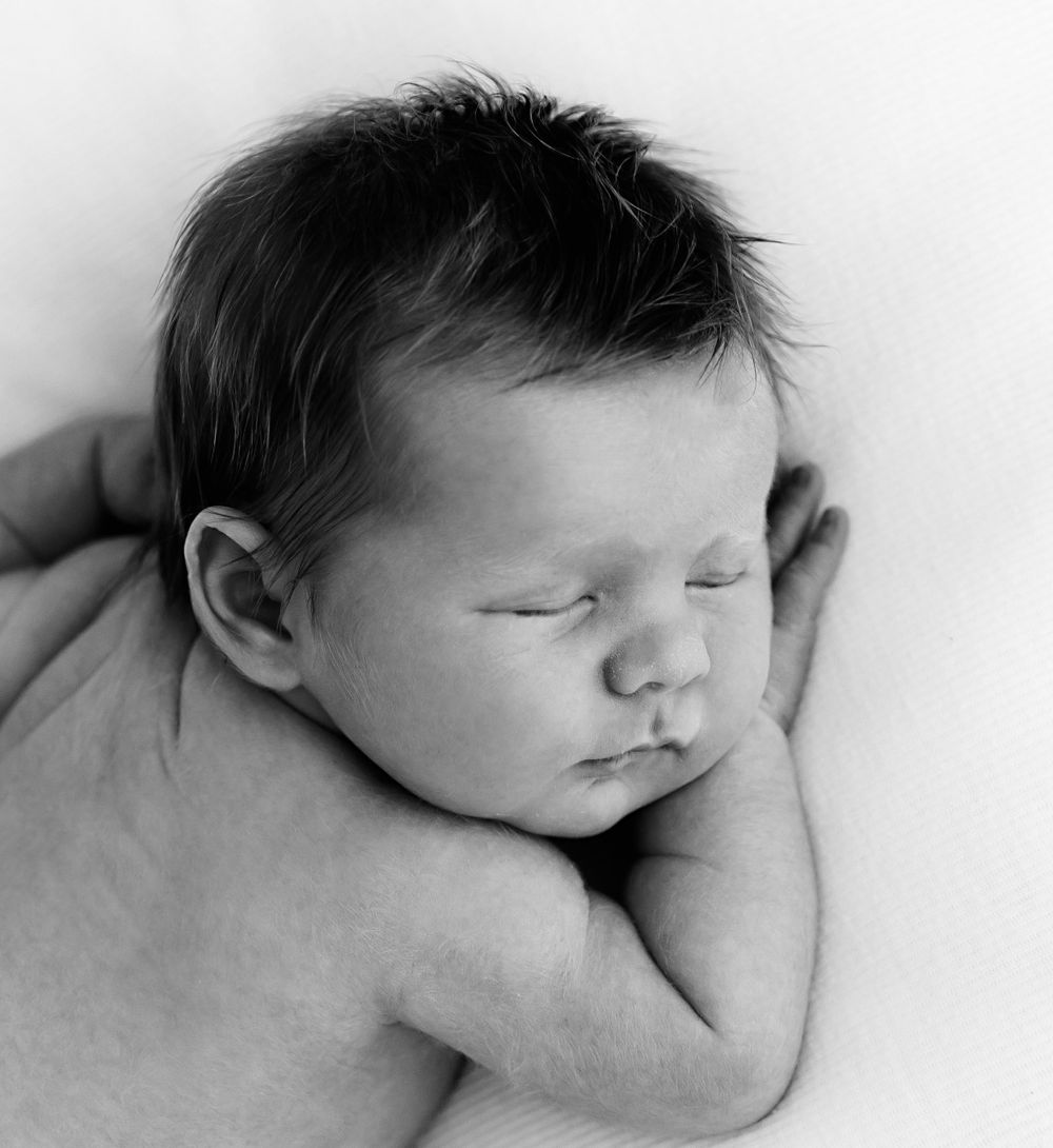 Gentle black and white portrait of sleeping newborn with dark hair against white backdrop.