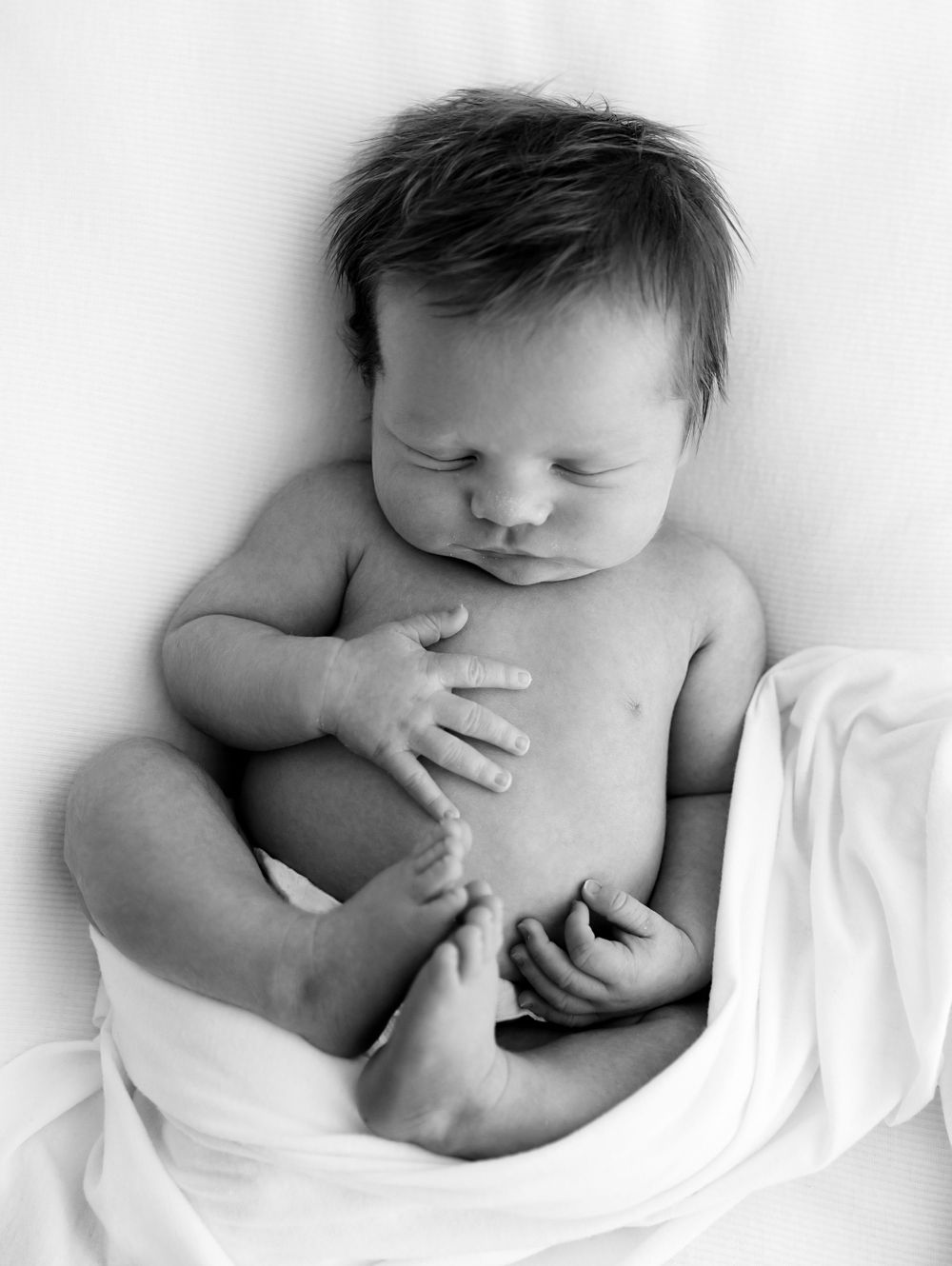 Artistic black and white photo of sleeping baby wrapped in white fabric.