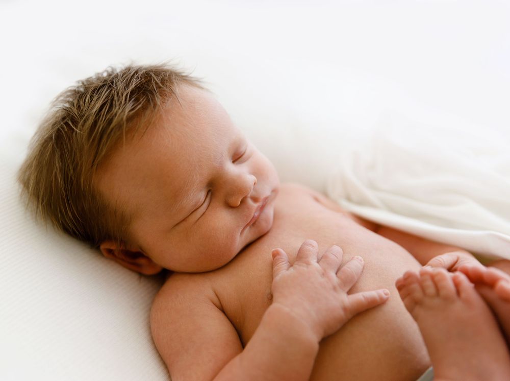 Serene portrait of sleeping newborn with soft hair resting against white background.
