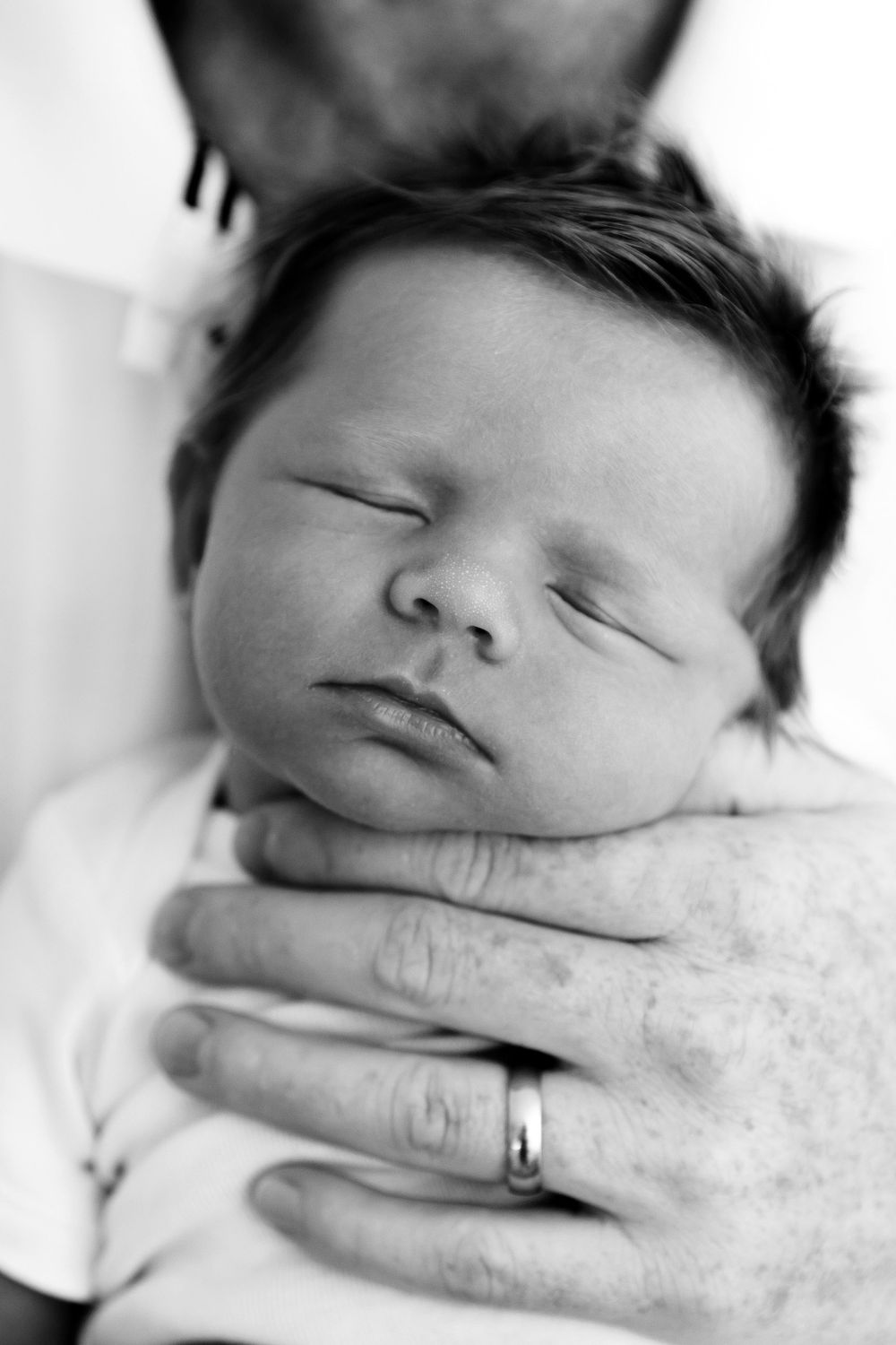 Close-up black and white image of a sleeping baby supported by adult hands.