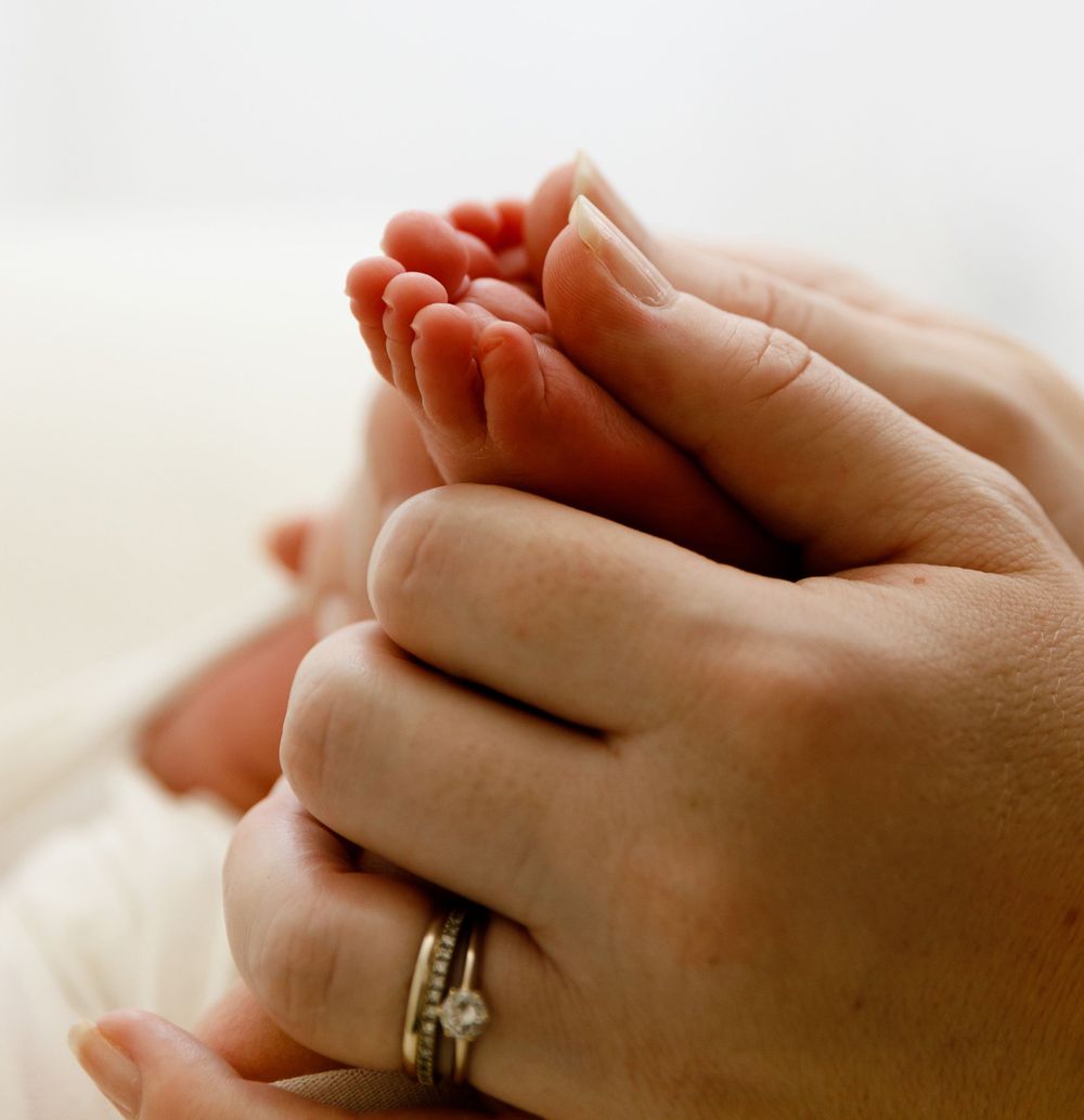 Close-up of hands wearing wedding rings holding tiny newborn feet.