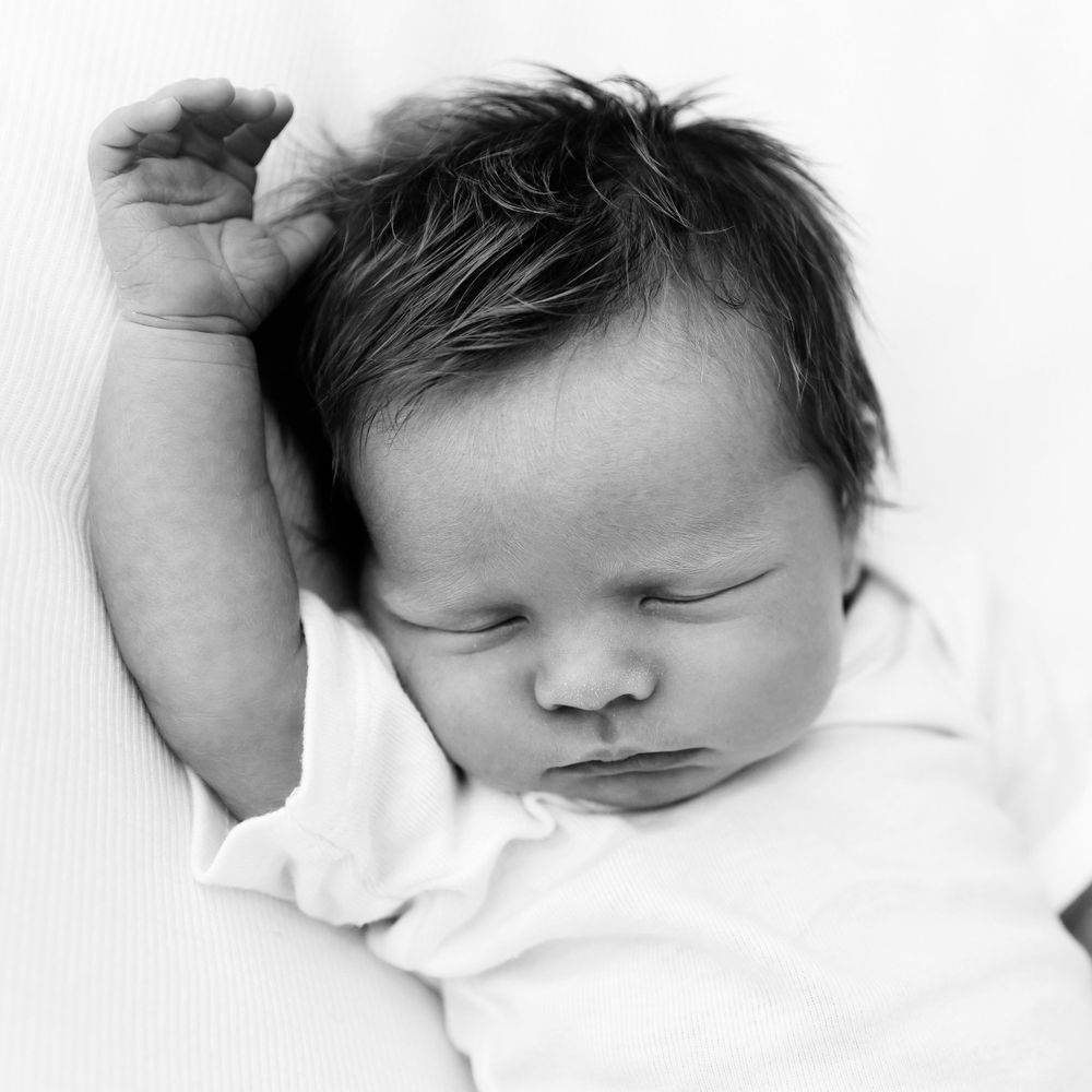 A black and white portrait of a sleeping newborn with messy hair against white backdrop.