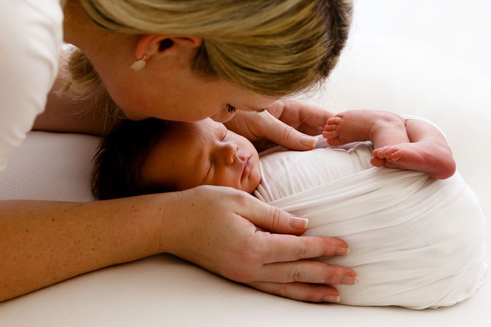 A tender moment showing a parent cuddling close to a sleeping newborn baby on white bedding.