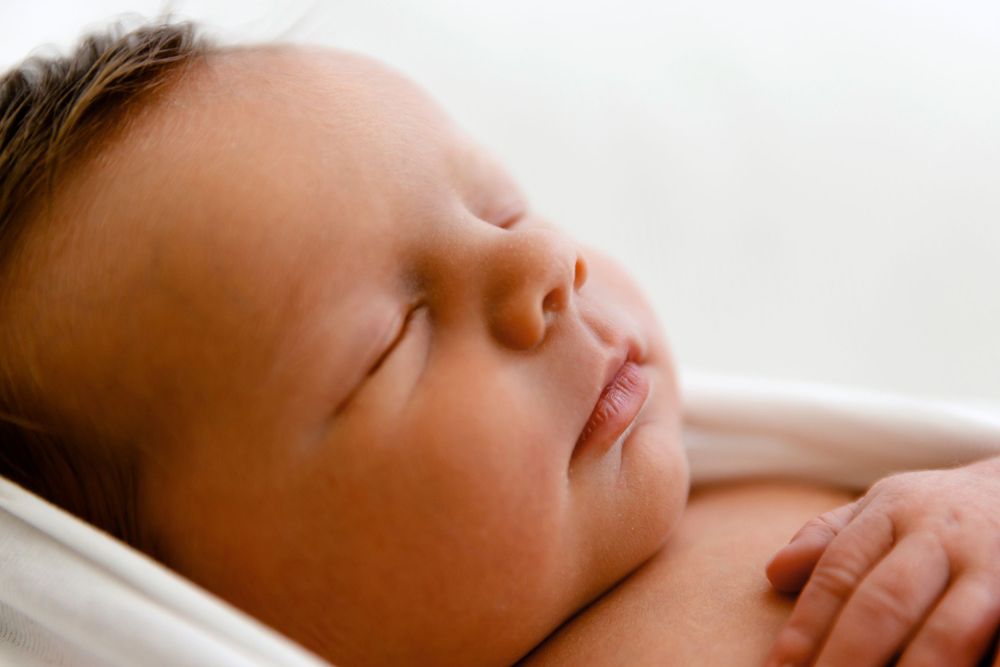 A peaceful sleeping newborn baby with chubby cheeks resting on white fabric.