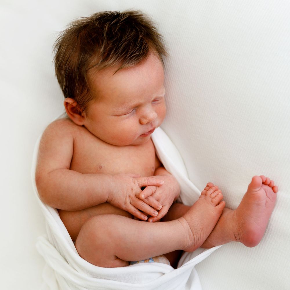 A naked newborn baby wrapped in white fabric with tiny feet visible.