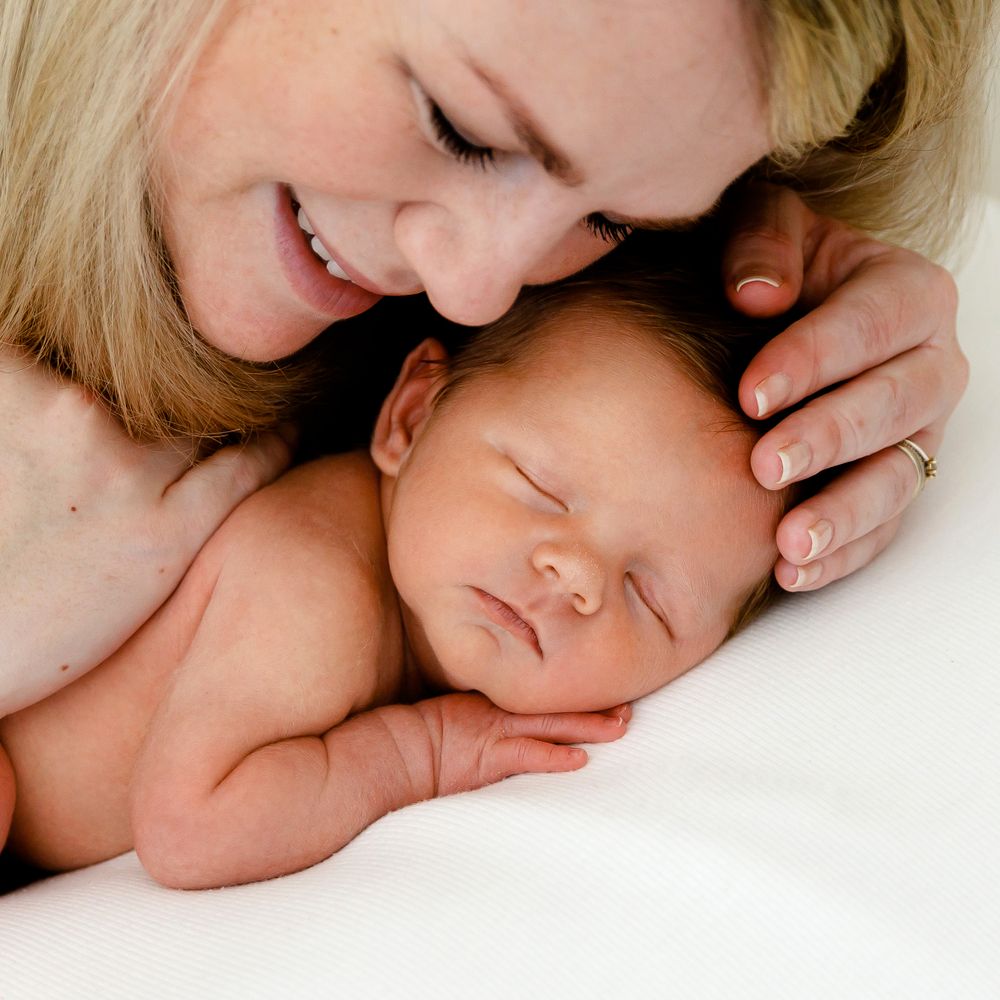 An intimate portrait of parent and newborn sharing a gentle moment on white bedding.