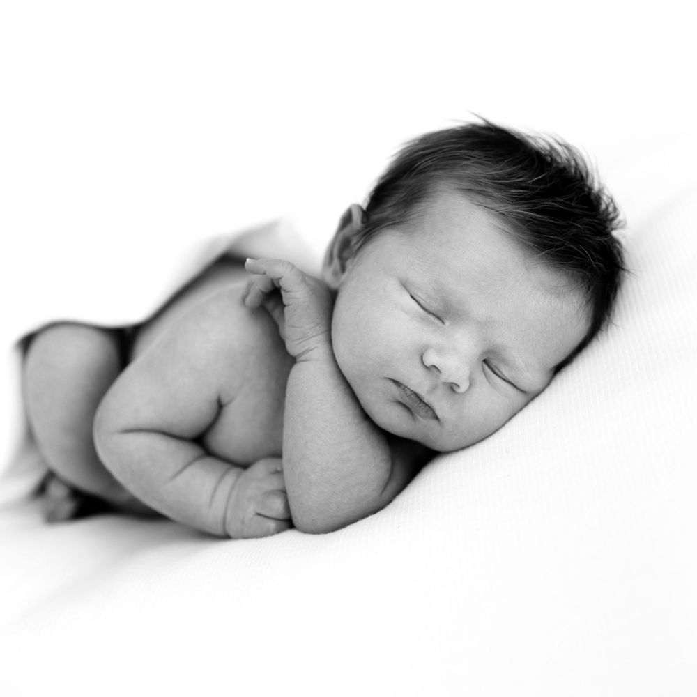 Black and white portrait of a sleeping newborn baby in a side-lying pose.