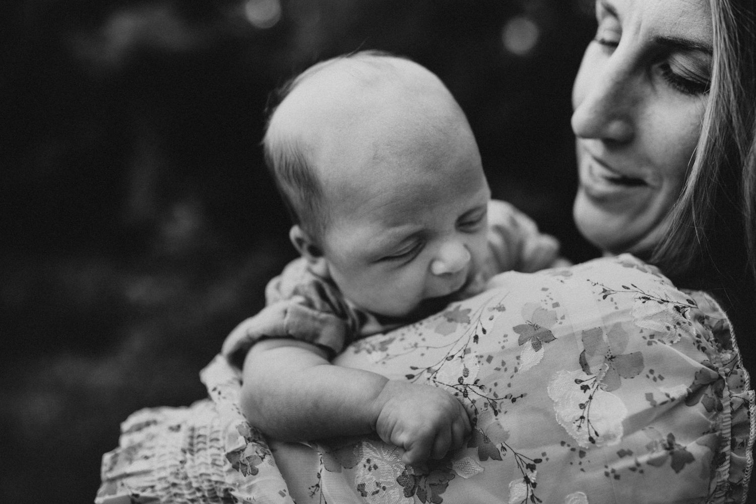 A tender black and white portrait of a sleeping newborn being held against floral fabric.