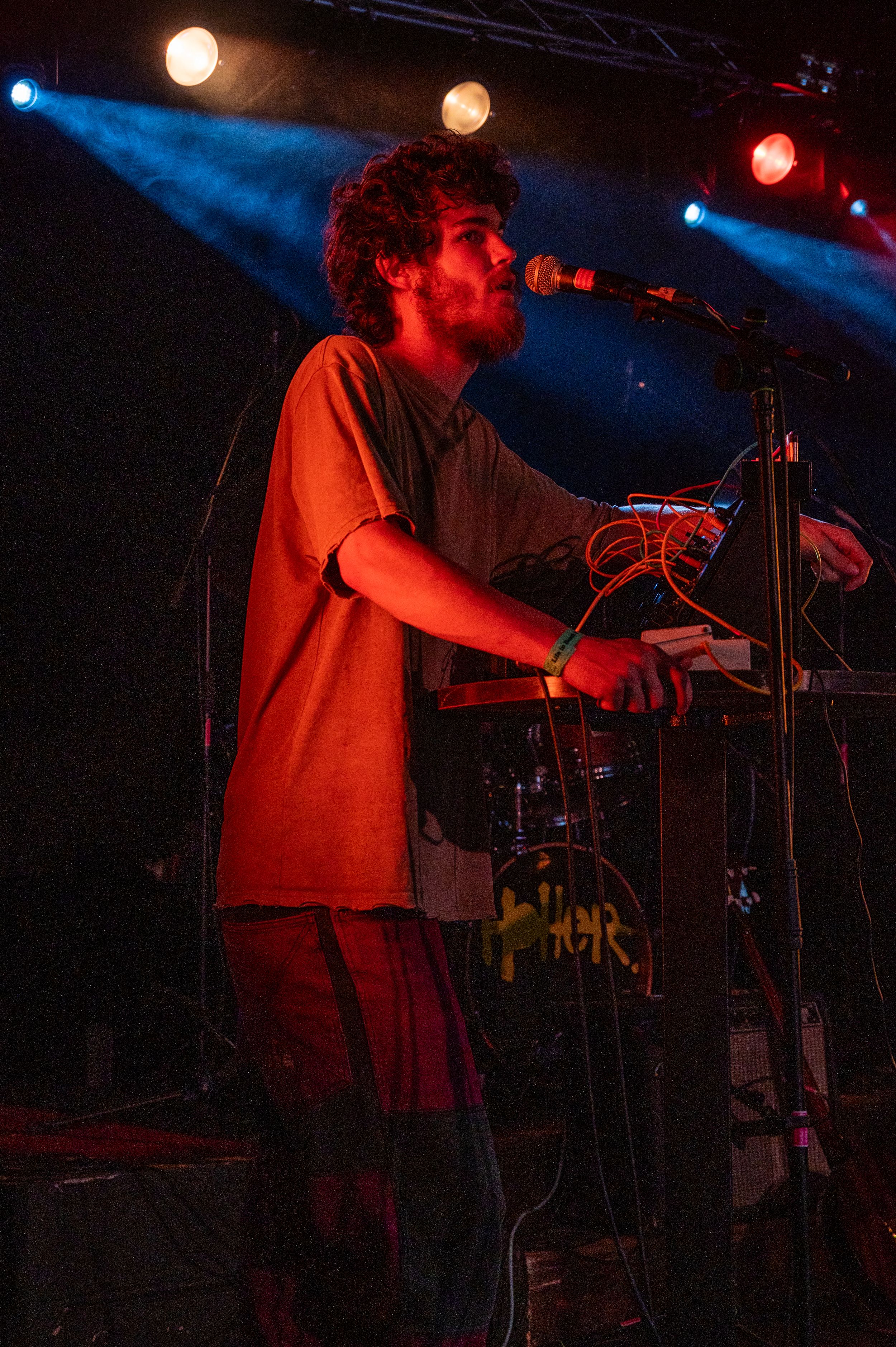 Musician performing with electronic equipment under dramatic red lighting on stage.