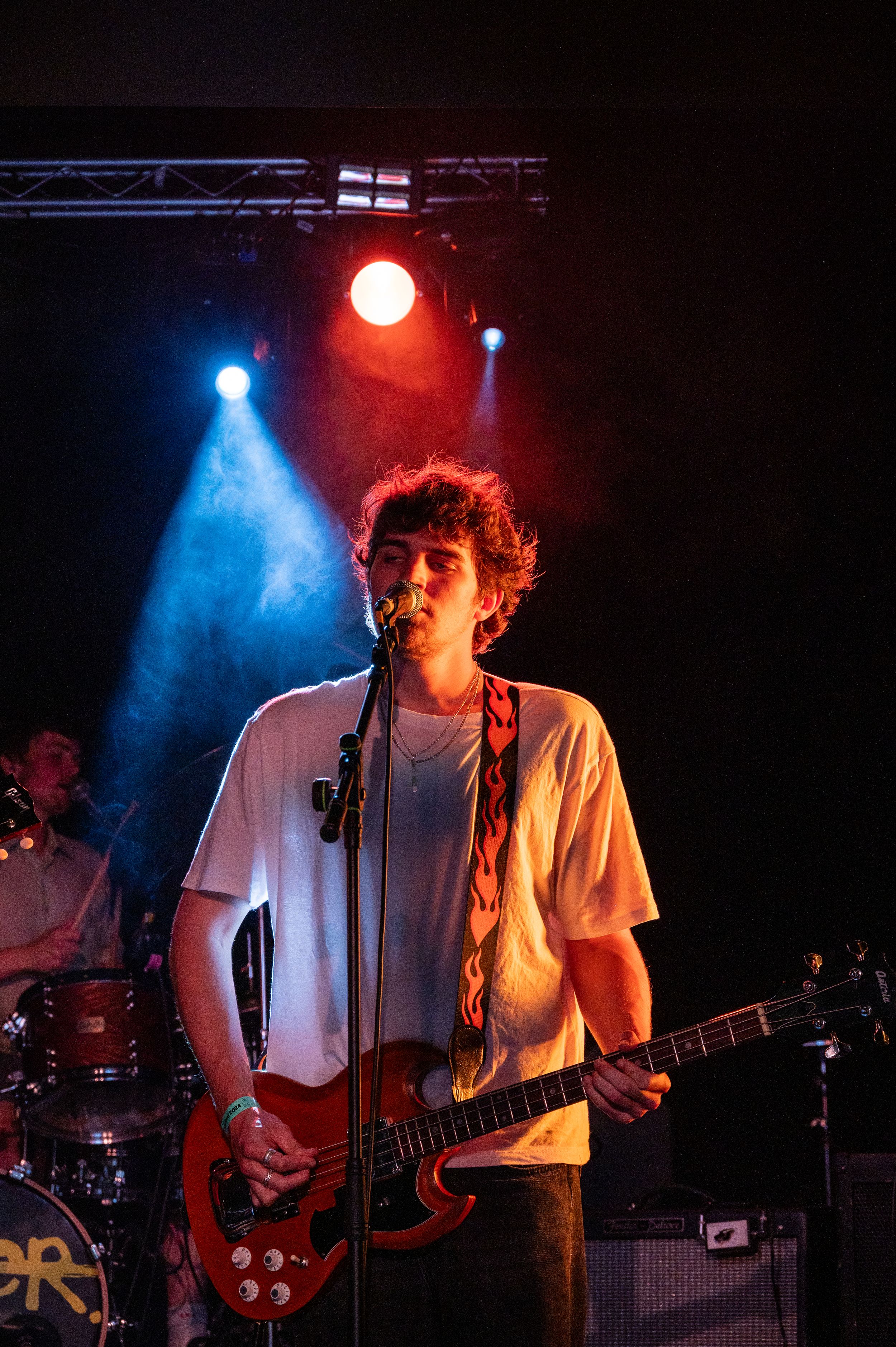 Guitarist in white t-shirt performs under vibrant red and blue stage lights during live concert.