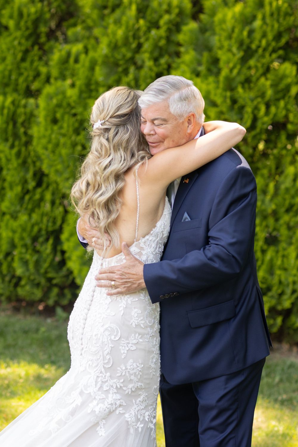 Emotional father-daughter embrace as bride in lace gown hugs older man in navy suit outdoors.