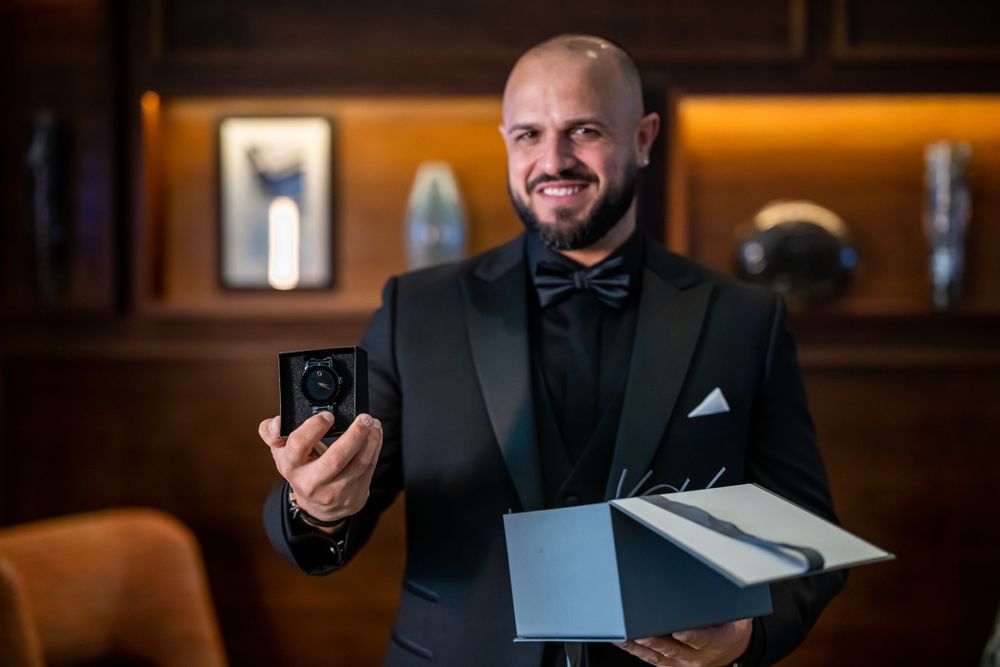 Groom in formal attire holding small box and documents in warmly lit room.
