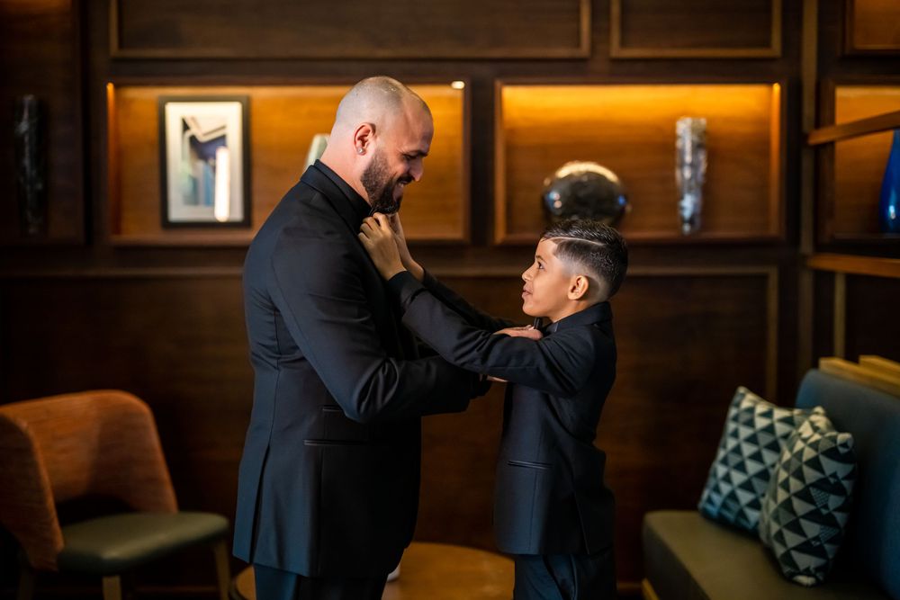 Two figures share an intimate moment in formal attire against wood-paneled walls with warm lighting.