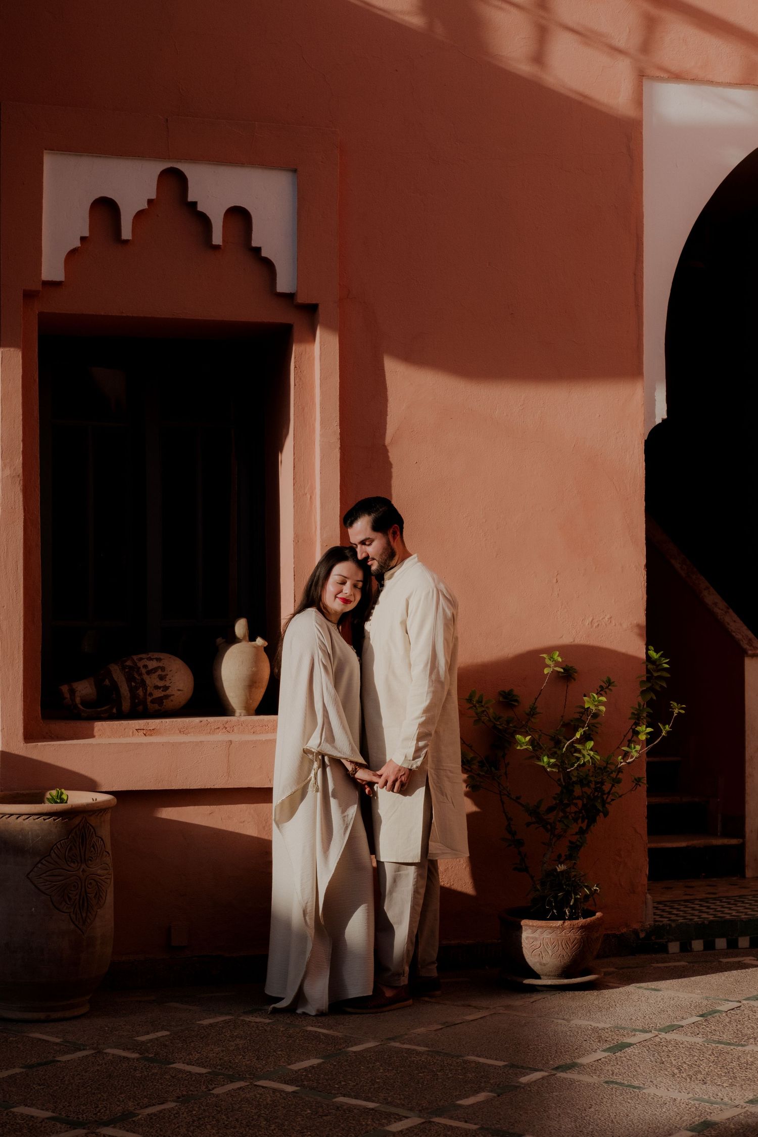 Couple in pink outfits posing against white modern building exterior.