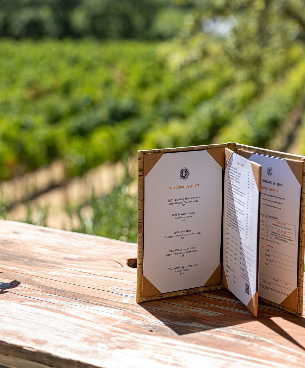 Restaurant menu holders displayed on wooden table with vineyard in background.