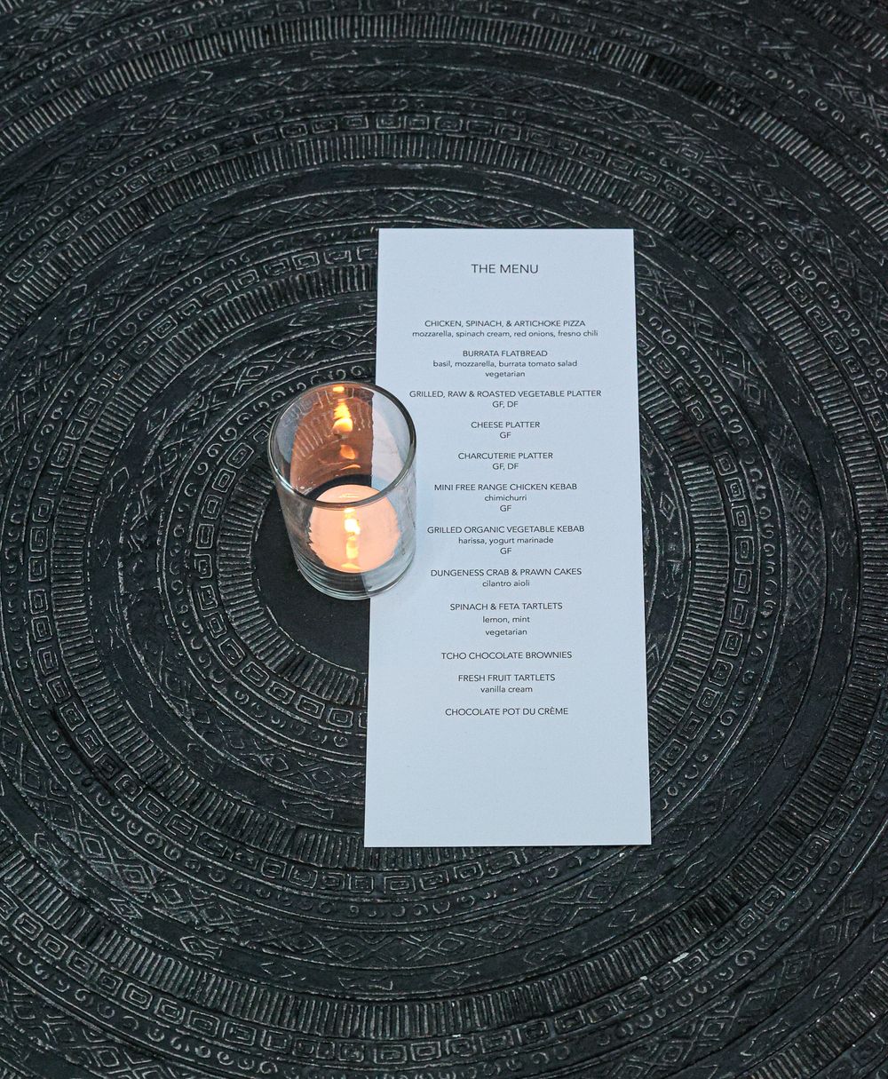 An event menu card placed next to a lit candle on a dark patterned surface.