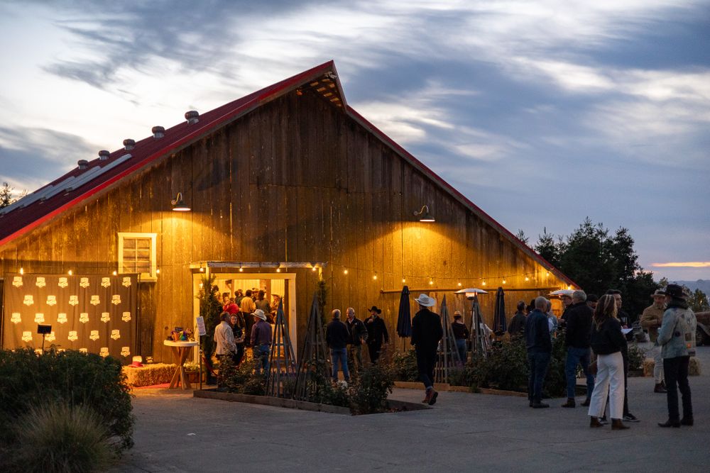 Rustic barn venue illuminated with warm lights hosts evening gathering of guests under twilight sky.