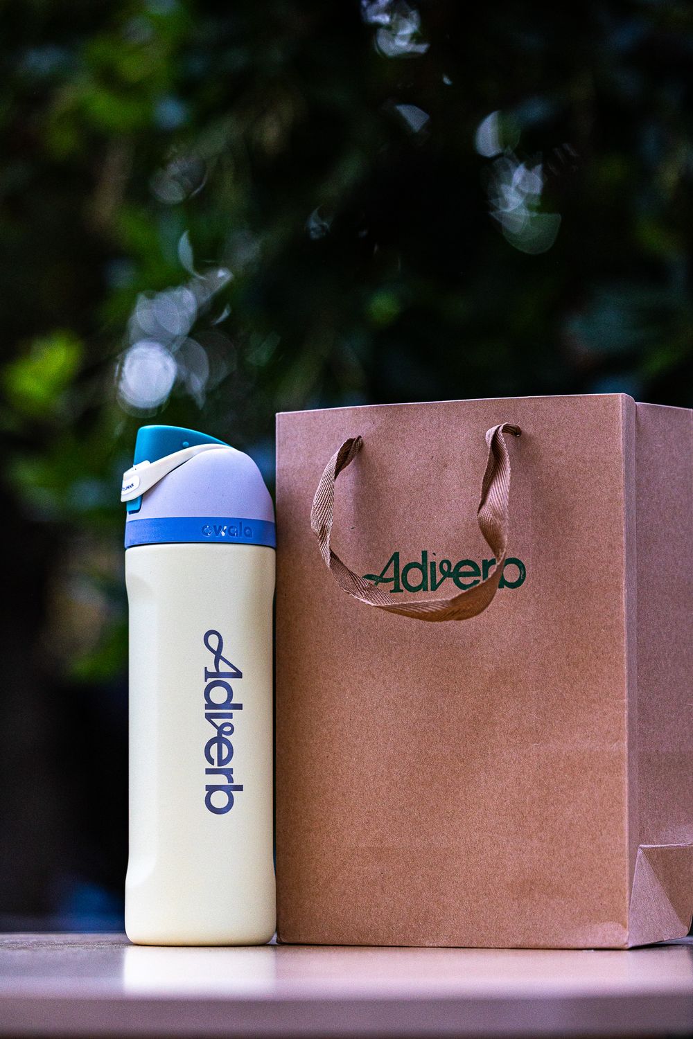 White water bottle and brown shopping bag with Adipero logo displayed on outdoor surface.