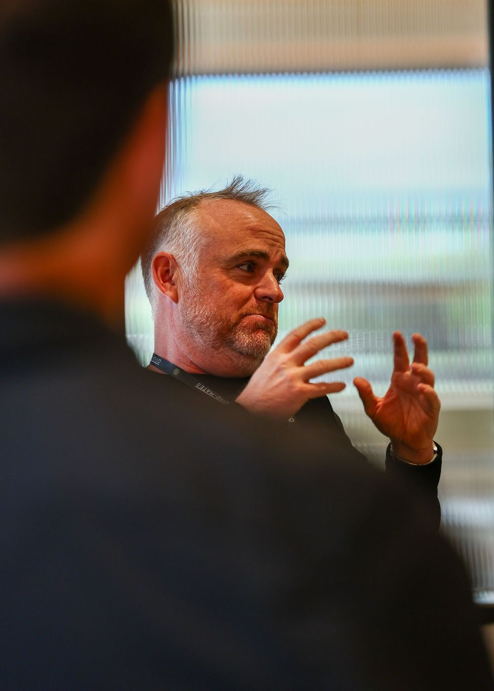 A person gestures animatedly while speaking during what appears to be a presentation or discussion in an indoor setting.