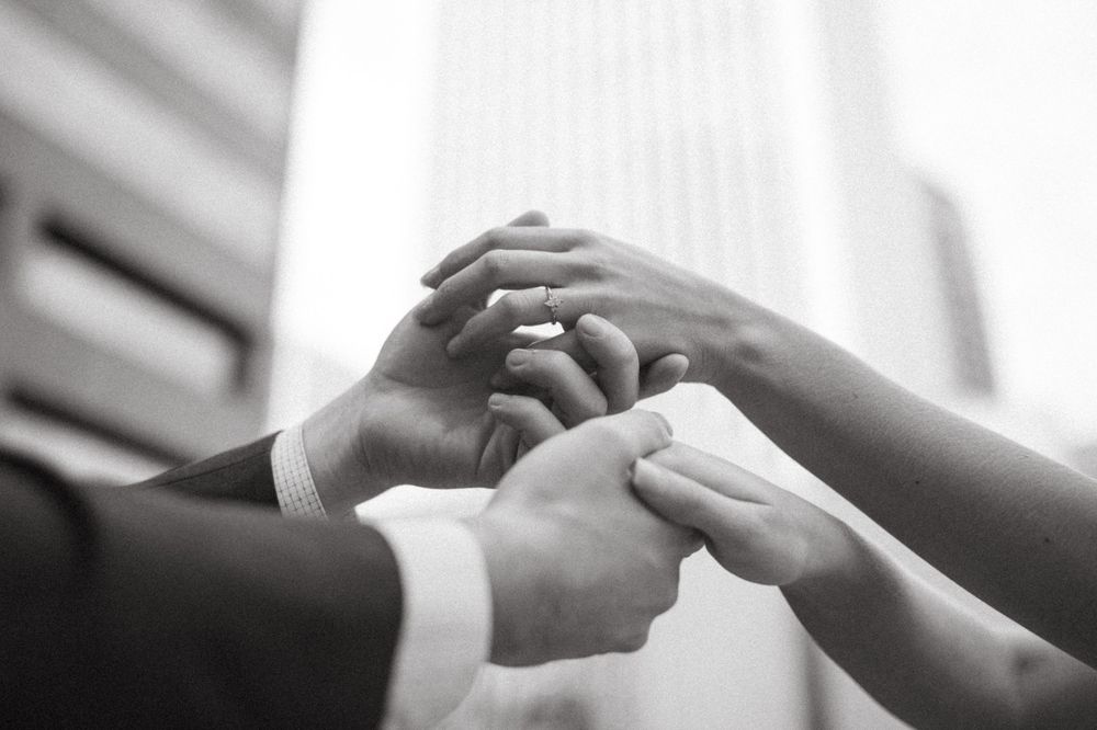 Black and white photo of diverse business team joining hands together in unity outdoors near modern building in Sacramento, California.