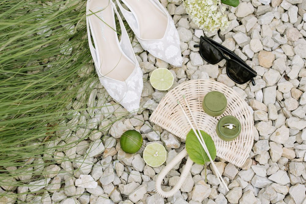 Flat lay of white lace shoes, wicker bag, sunglasses, limes, and green drinks on white pebbles in Sacramento, California.
