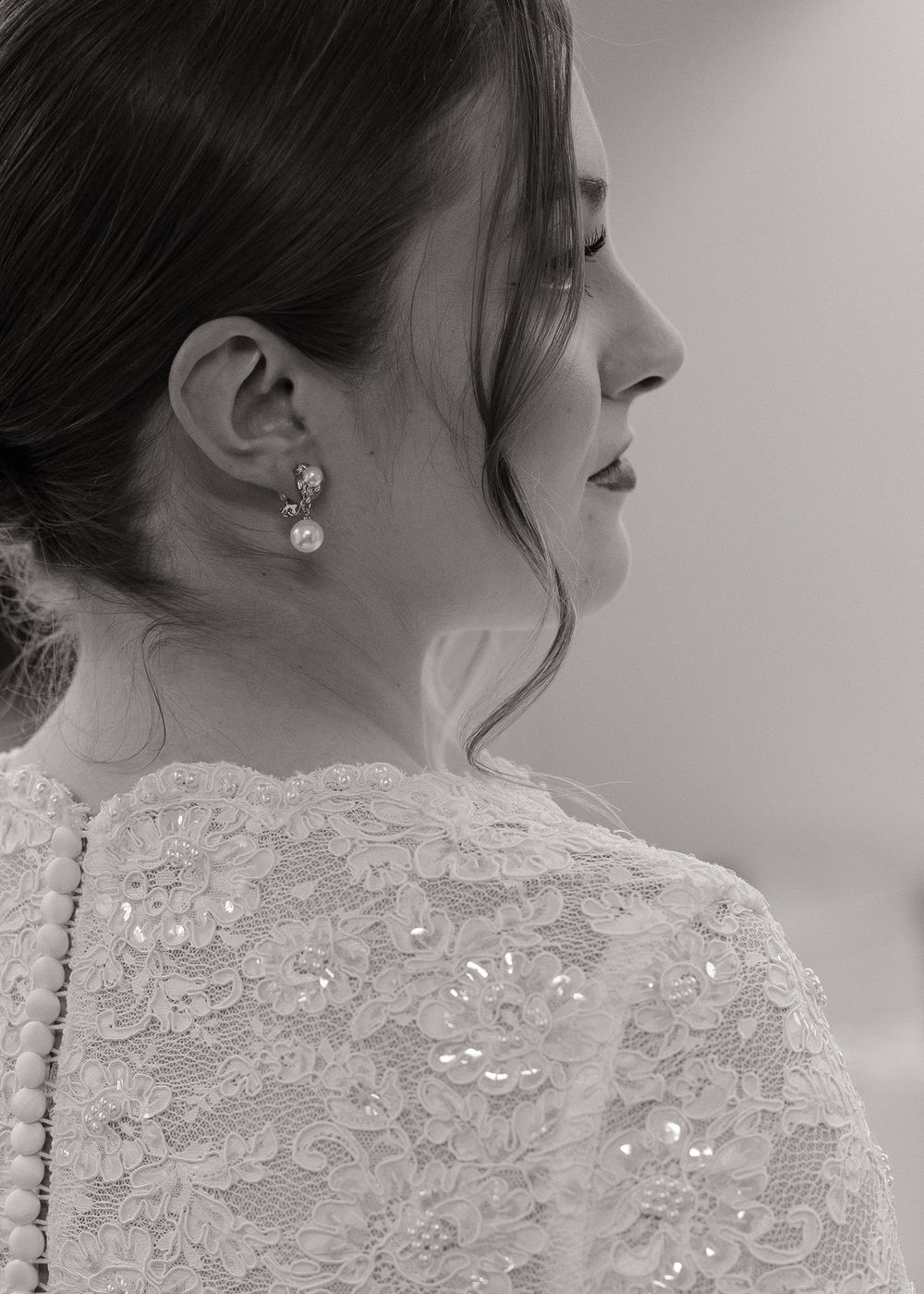 Black and white profile portrait of a bride in lace gown with pearl drop earrings, hair elegantly styled up.