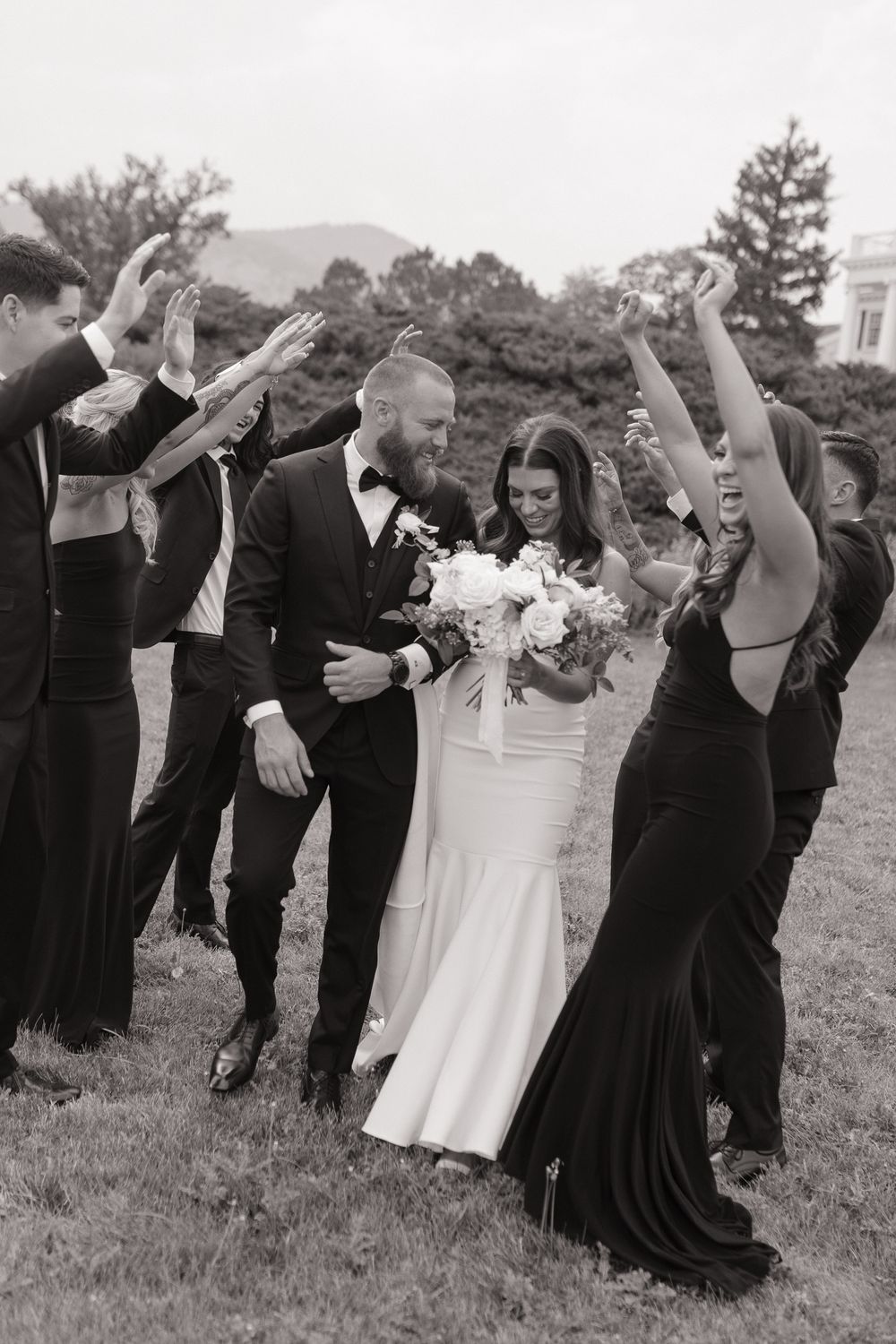 Black and white wedding photo of bride and groom walking through cheering bridal party tunnel outdoors in Sacramento, California.