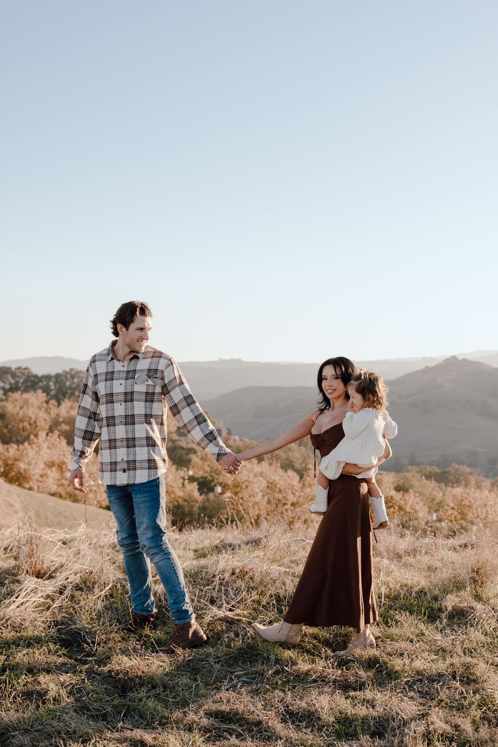 A couple dances together on a hilltop during golden hour in a romantic outdoor photoshoot.