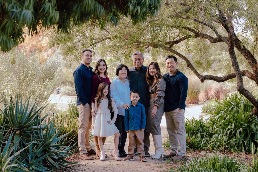 Group of people gathered outdoors for family photo under tree branches.