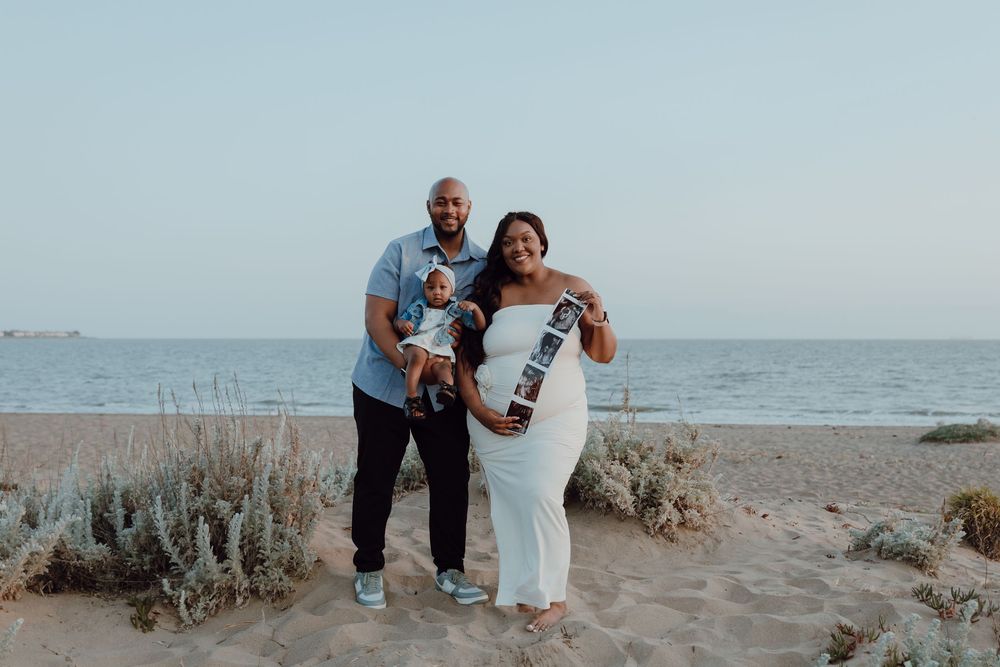 Couple in wedding attire walking together on a sandy beach with ocean waves in the background.