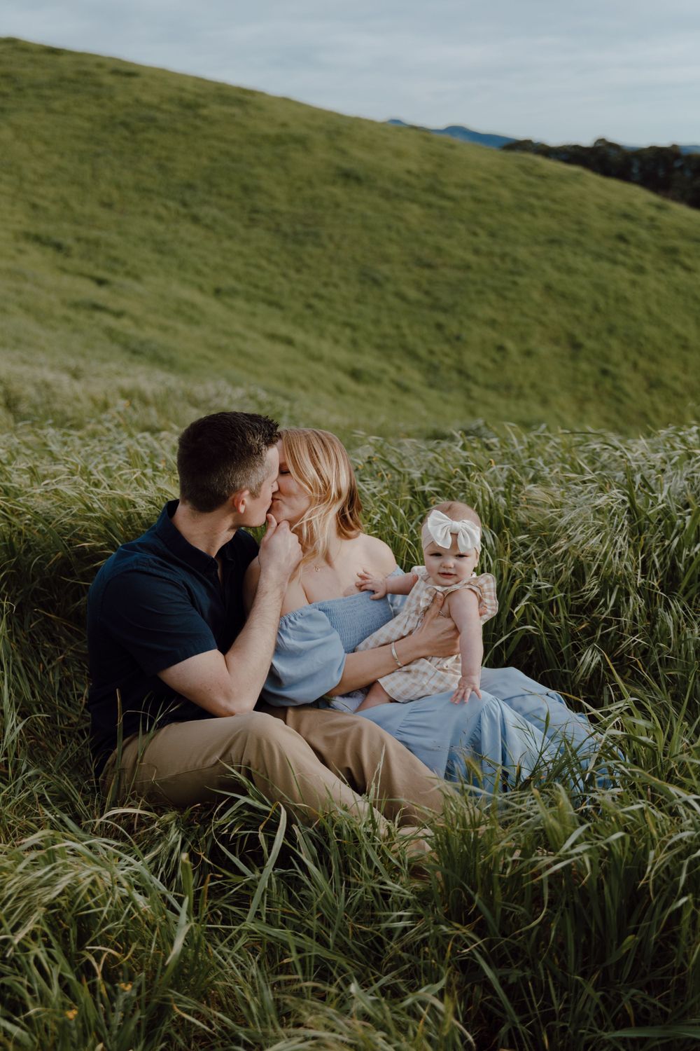 Family sharing intimate moment while sitting in tall grass on hillside.