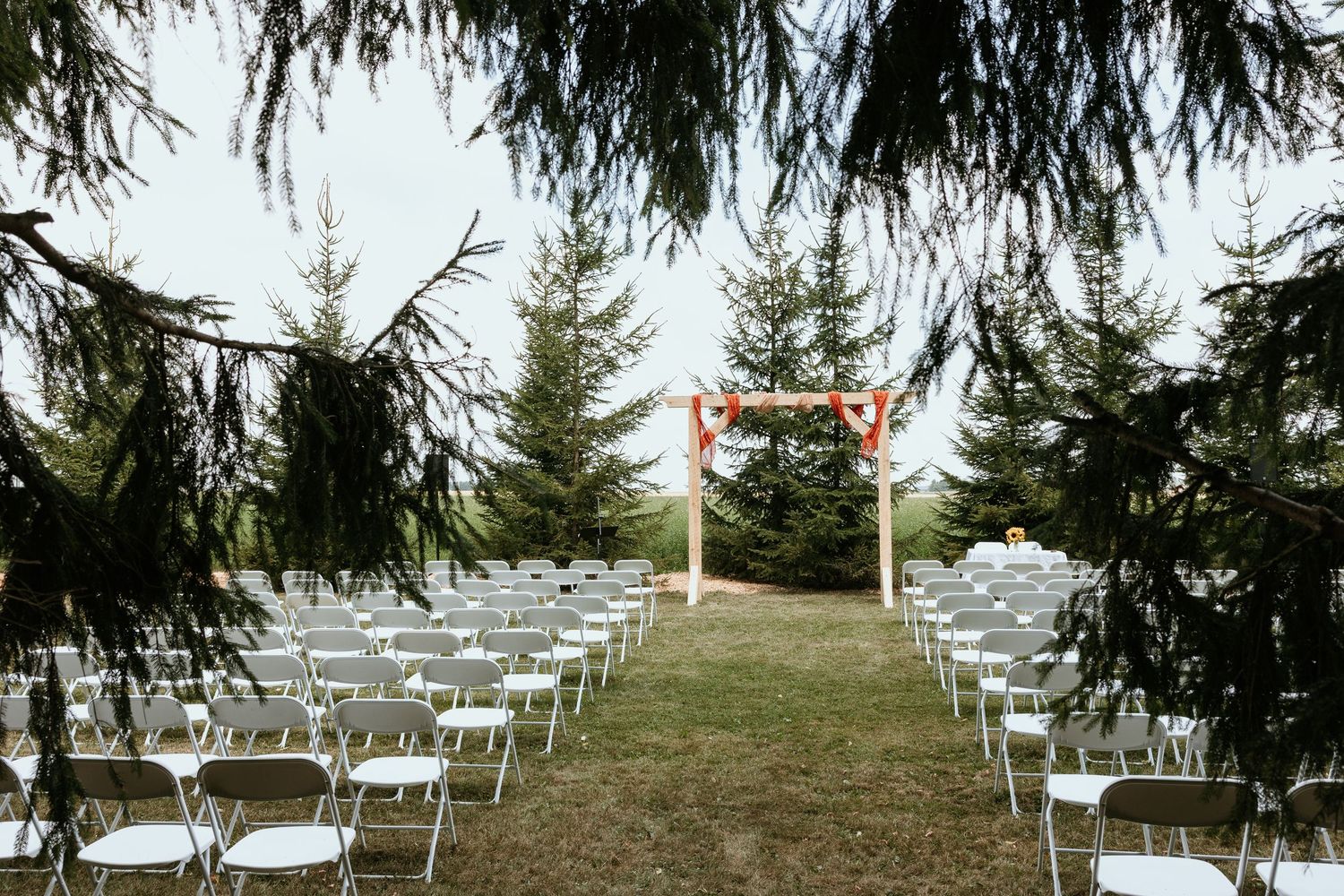 White folding chairs arranged in rows on a grassy hillside for an outdoor wedding ceremony under evergreen trees.