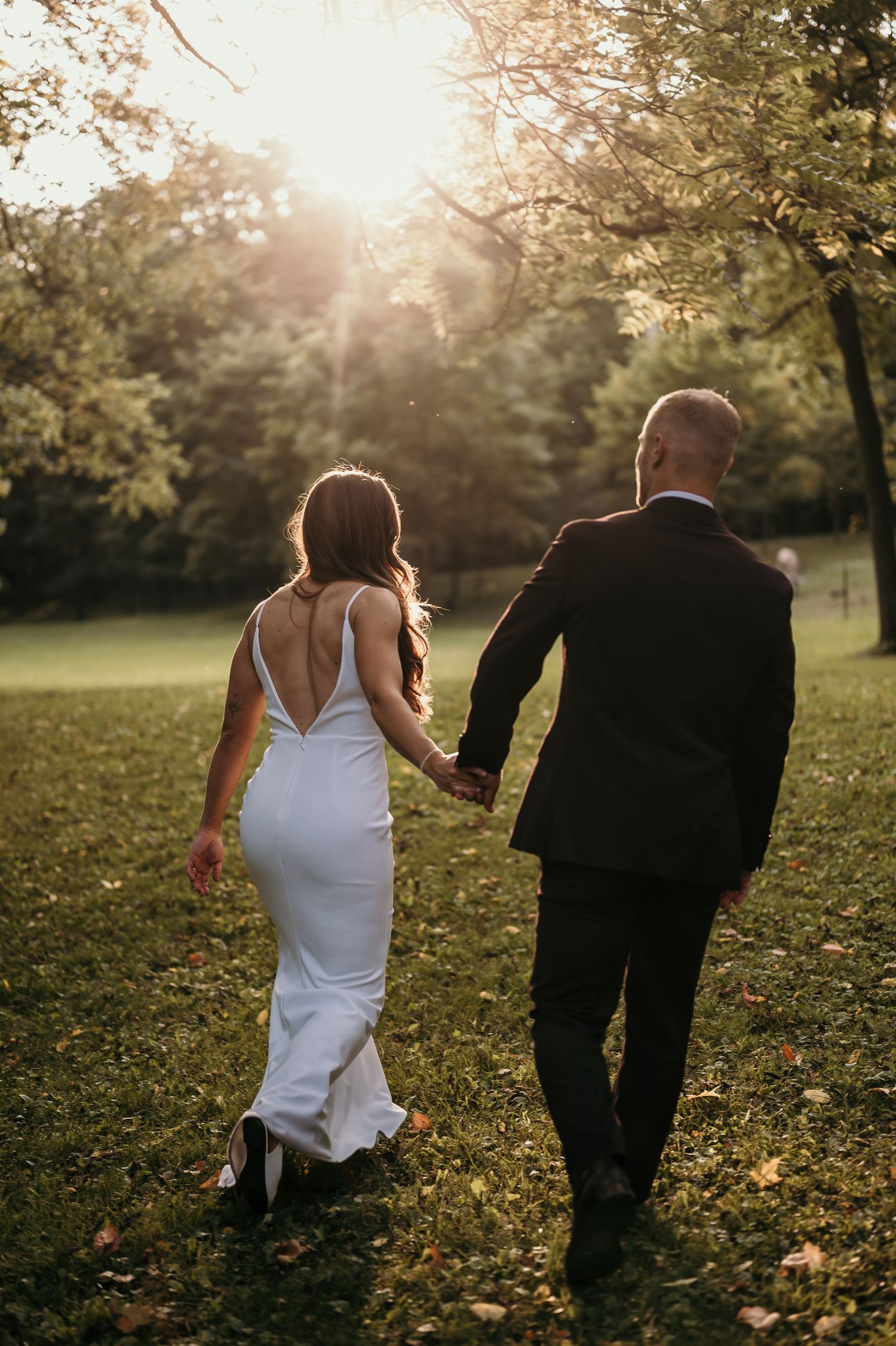 Newlyweds walk hand in hand through a sunlit garden during golden hour.