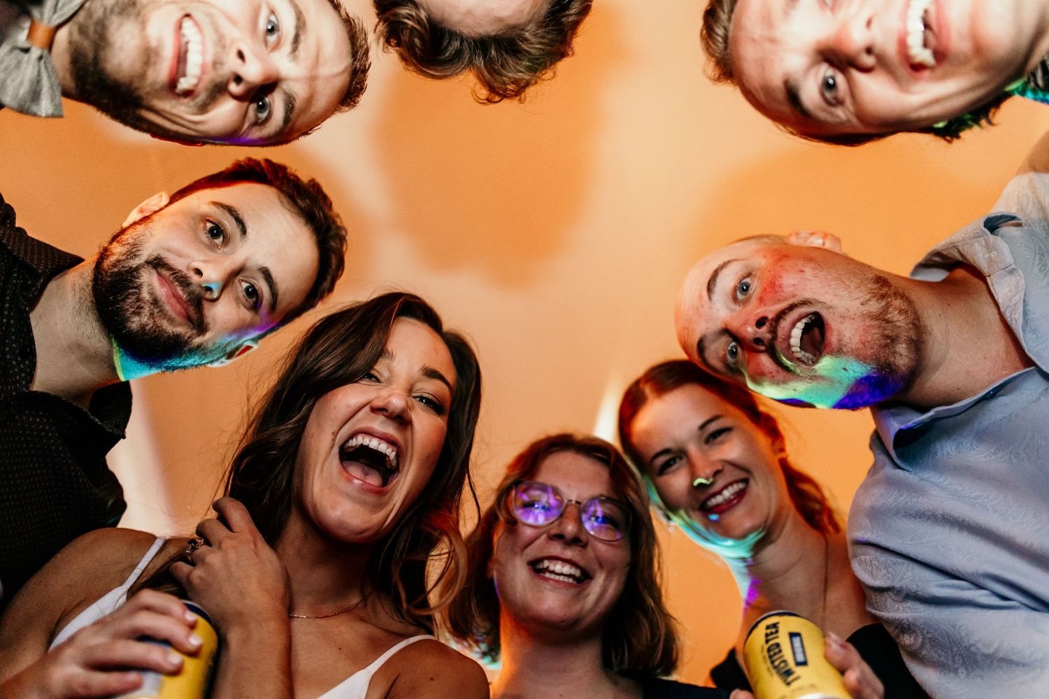 Group of friends form circle looking down at camera with excited expressions.